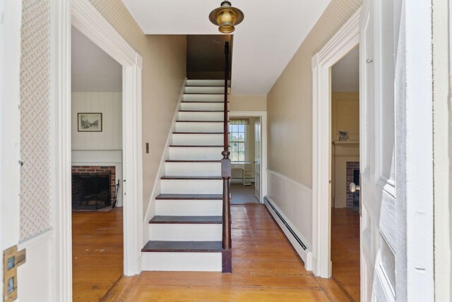 538 Malbons Mills Rd, Skowhegan, ME 04976 - stairs featuring baseboard heating, wallpapered walls, a fireplace, a wainscoted wall, and wood finished floors