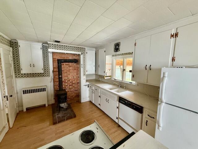 kitchen featuring white appliances, radiator, a wood stove, light wood-type flooring, and light countertops