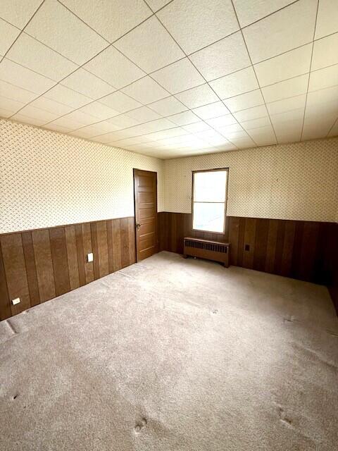 spare room with radiator heating unit, wallpapered walls, a wainscoted wall, carpet floors, and wood walls