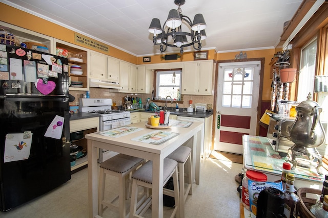 kitchen featuring freestanding refrigerator, under cabinet range hood, ornamental molding, a chandelier, and dark countertops