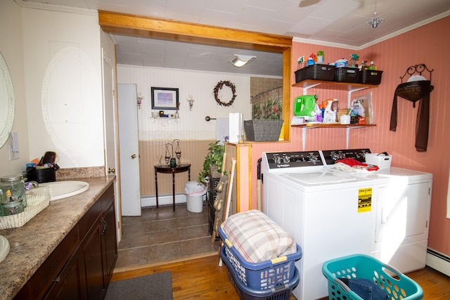 clothes washing area with washer and clothes dryer, baseboard heating, ornamental molding, and wood finished floors