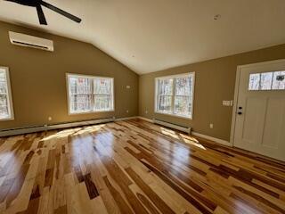 29 Sunnybrook Farm Rd, Bridgton, ME 04009 - unfurnished living room with vaulted ceiling, a wall unit AC, healthy amount of natural light, wood finished floors, and baseboard heating