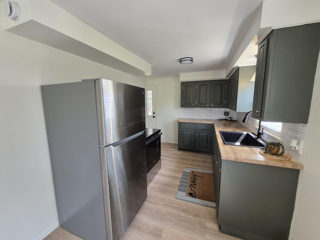 kitchen with freestanding refrigerator, a sink, butcher block countertops, decorative backsplash, and light wood-style floors
