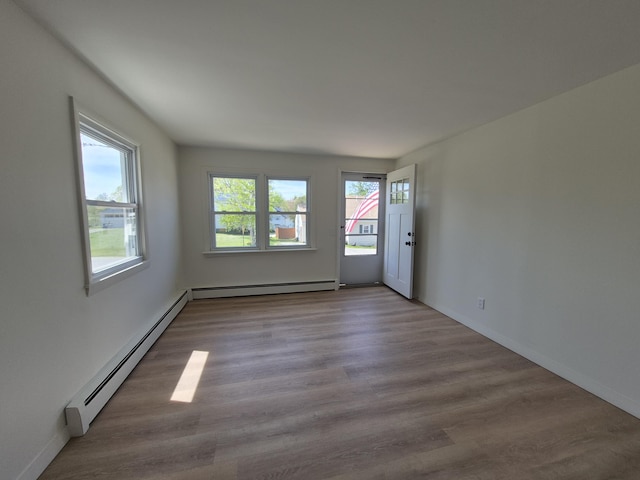 unfurnished room with a baseboard radiator, wood finished floors, and baseboards