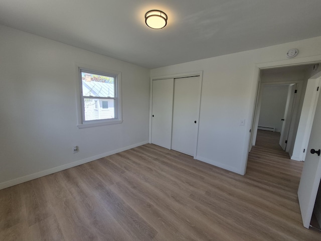 unfurnished bedroom featuring a baseboard heating unit, baseboards, wood finished floors, and a closet