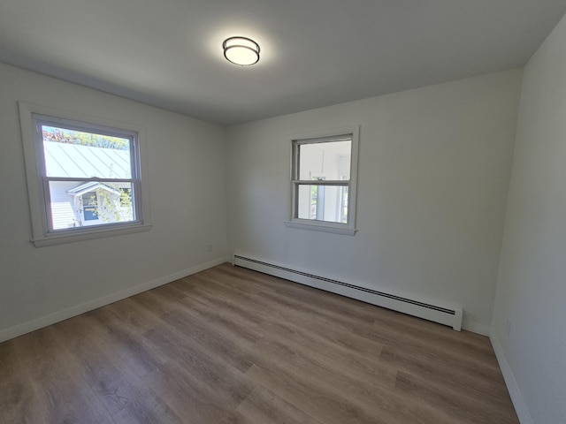unfurnished room with a baseboard heating unit, plenty of natural light, wood finished floors, and baseboards
