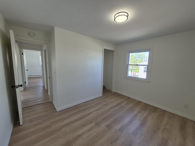 empty room featuring a baseboard heating unit, light wood-style flooring, baseboards, and a smoke detector