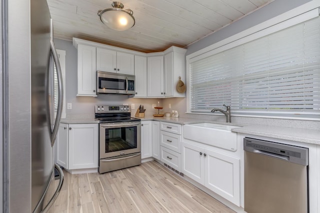 kitchen featuring stainless steel appliances, a sink, light wood-type flooring, white cabinets, and plenty of natural light