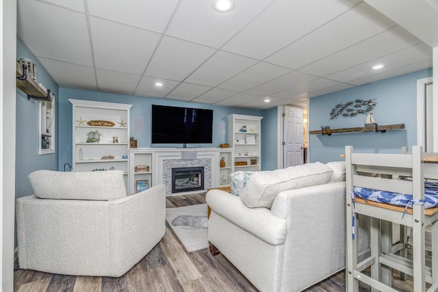 living room featuring wood finished floors, a paneled ceiling, a glass covered fireplace, and recessed lighting
