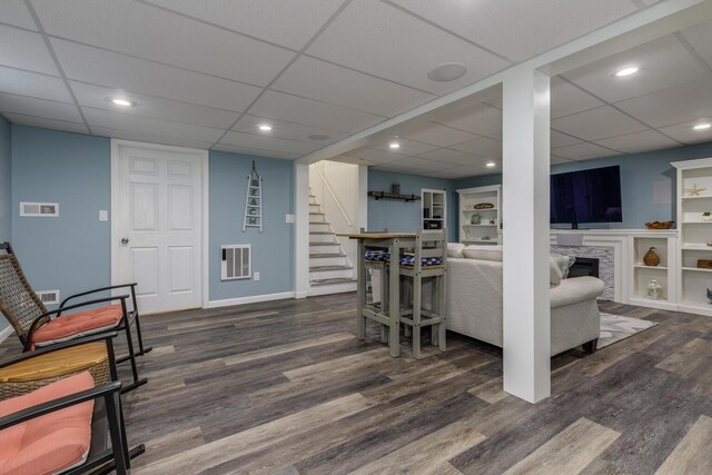 living area featuring stairway, wood finished floors, a fireplace, a paneled ceiling, and baseboards