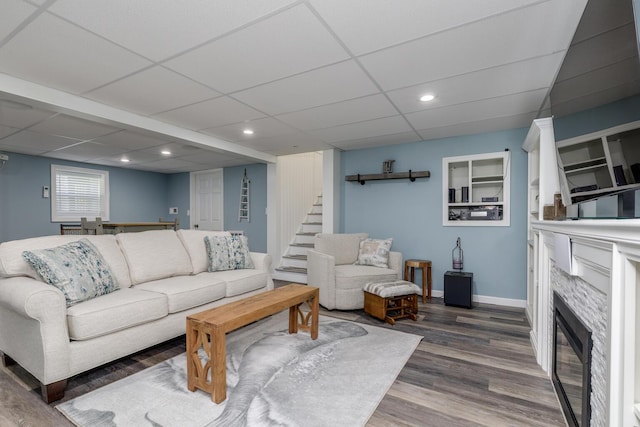 living area featuring a tile fireplace, wood finished floors, baseboards, recessed lighting, and a paneled ceiling