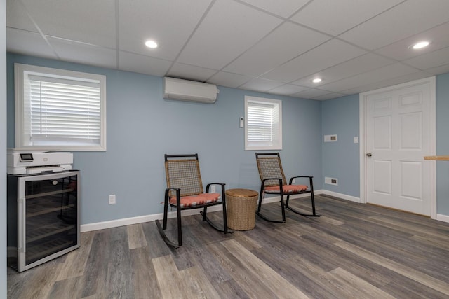 sitting room featuring wine cooler, a wall mounted air conditioner, a paneled ceiling, wood finished floors, and baseboards