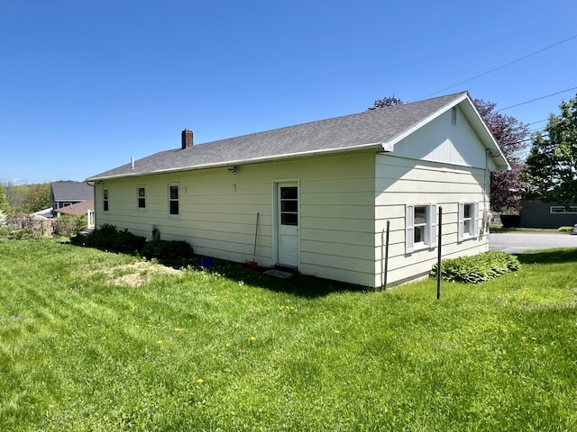 view of property exterior with a chimney, a yard, and a shingled roof