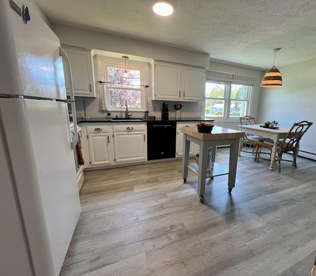kitchen featuring freestanding refrigerator, black dishwasher, a sink, dark countertops, and light wood-style floors