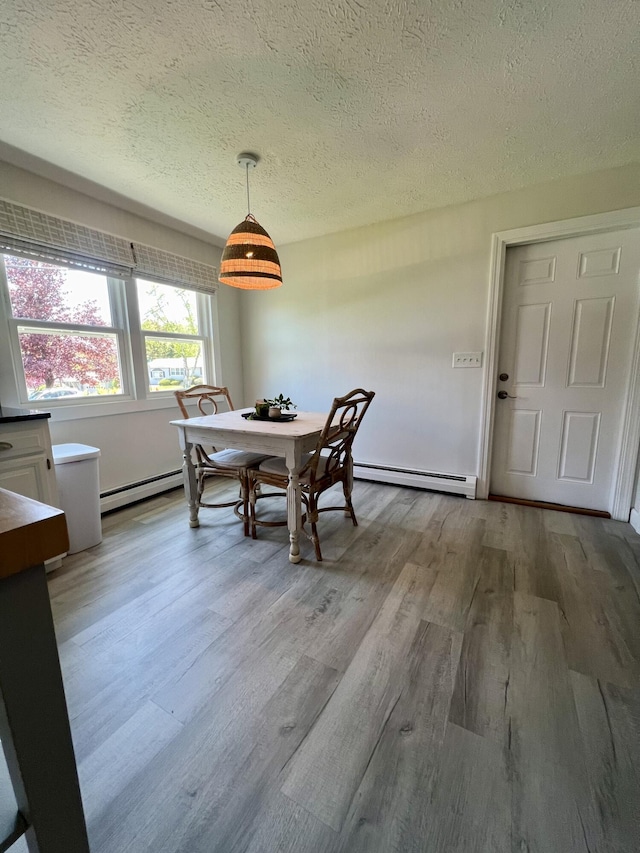 dining space featuring baseboard heating, wood finished floors, and a textured ceiling