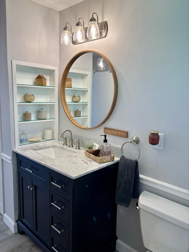 bathroom with toilet, vanity, wood finished floors, and baseboards