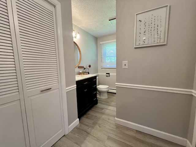 bathroom featuring toilet, wood finished floors, baseboard heating, a textured ceiling, and vanity