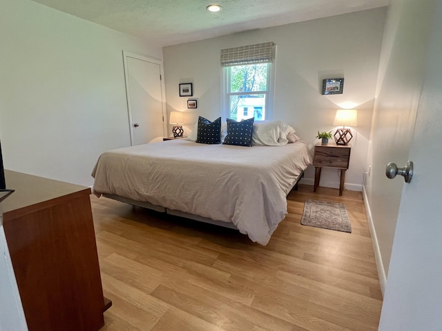 bedroom with light wood finished floors, baseboards, and a textured ceiling