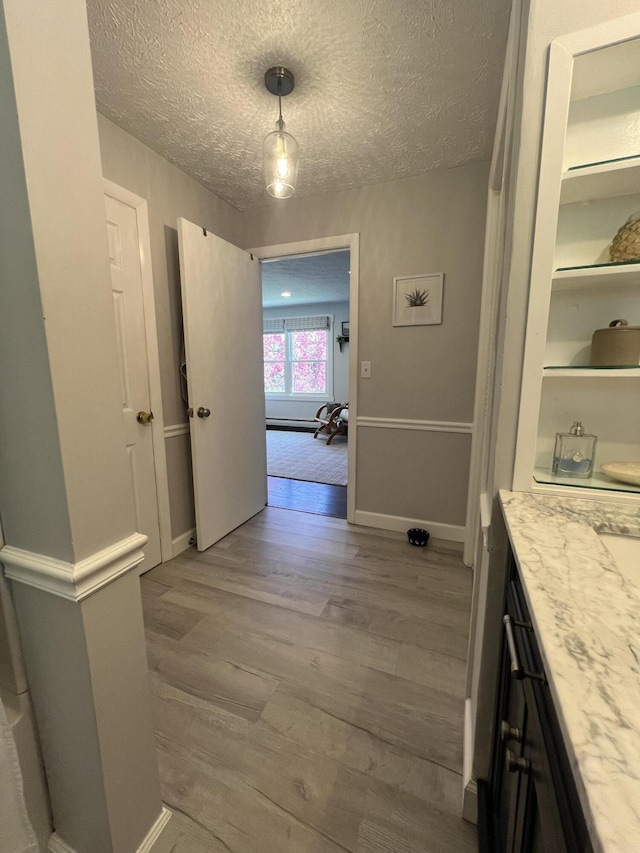 corridor with wood finished floors, a textured ceiling, and baseboards