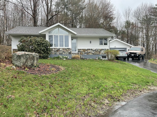 view of front of house featuring stone siding, a front lawn, an outbuilding, and roof with shingles