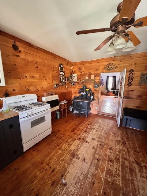 kitchen with white gas stove, a wood stove, wood-type flooring, wooden walls, and ceiling fan