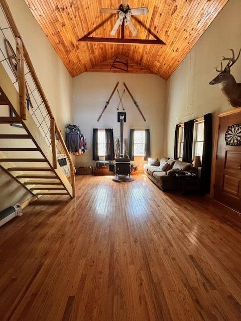 living area with high vaulted ceiling, wooden ceiling, a wood stove, wood finished floors, and ceiling fan
