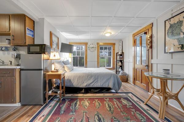 bedroom with freestanding refrigerator, light wood finished floors, and multiple windows