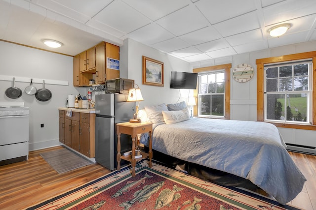 bedroom with freestanding refrigerator, light wood-type flooring, and baseboards