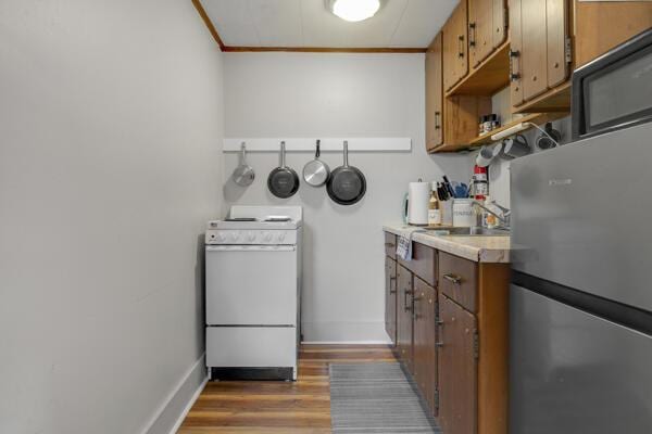 kitchen with white stove, freestanding refrigerator, ornamental molding, light countertops, and a sink