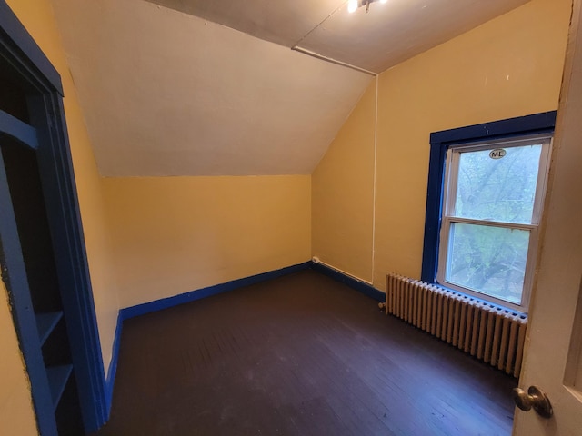 additional living space featuring radiator, vaulted ceiling, dark wood finished floors, and baseboards