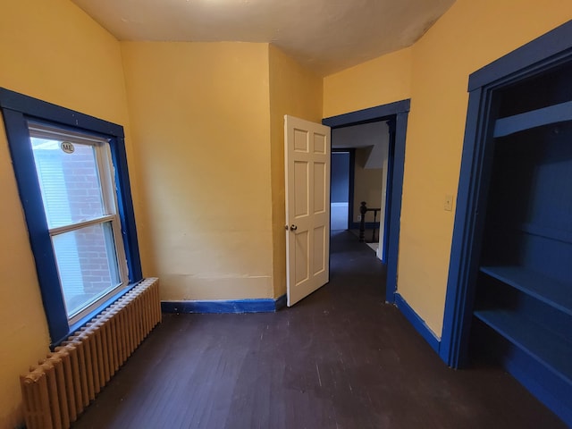 unfurnished bedroom with radiator heating unit, baseboards, and wood finished floors