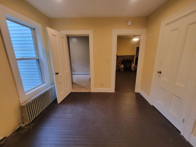 corridor featuring radiator heating unit, baseboard heating, dark wood-type flooring, and baseboards
