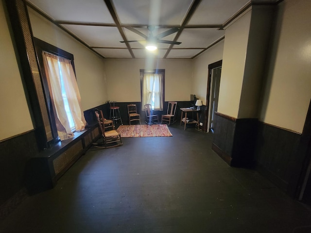 sitting room with wainscoting, a ceiling fan, and concrete flooring