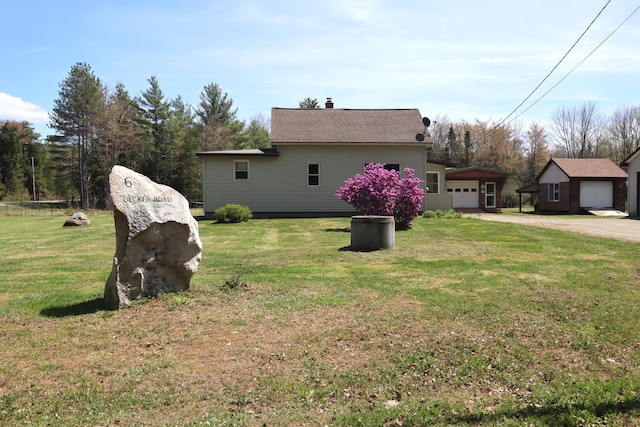 view of home's exterior featuring a detached garage, a chimney, a lawn, and driveway