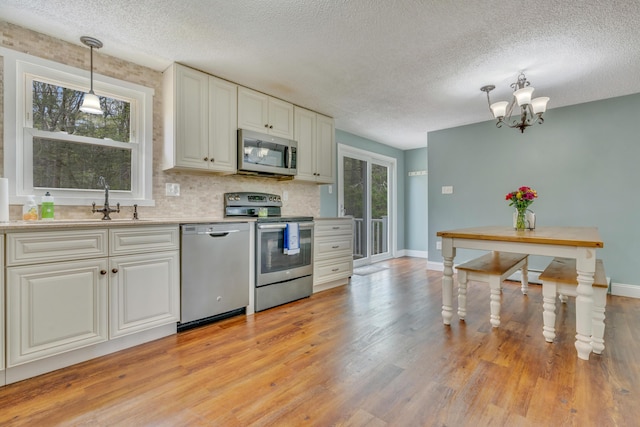 kitchen with stainless steel appliances, a textured ceiling, light wood finished floors, a chandelier, and light countertops