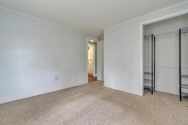 unfurnished bedroom with carpet flooring, ornamental molding, a closet, baseboards, and a textured ceiling