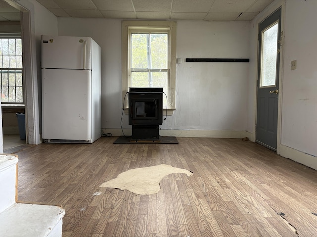 43 Berry Mills Rd, Carthage, ME 04224 - unfurnished living room with a paneled ceiling, light wood finished floors, a wood stove, plenty of natural light, and baseboards