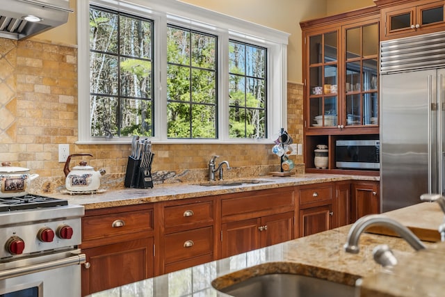 1026 Essex St, Bangor, ME 04401 - kitchen featuring premium appliances, exhaust hood, brown cabinetry, light stone countertops, and glass insert cabinets