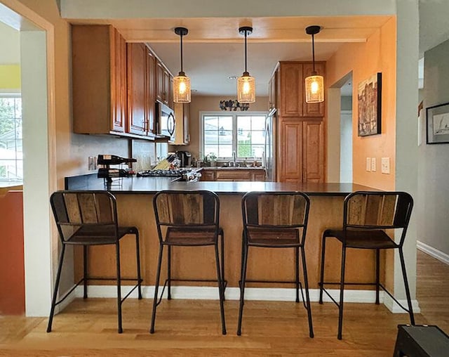 kitchen with a peninsula, brown cabinets, light wood-type flooring, and dark countertops
