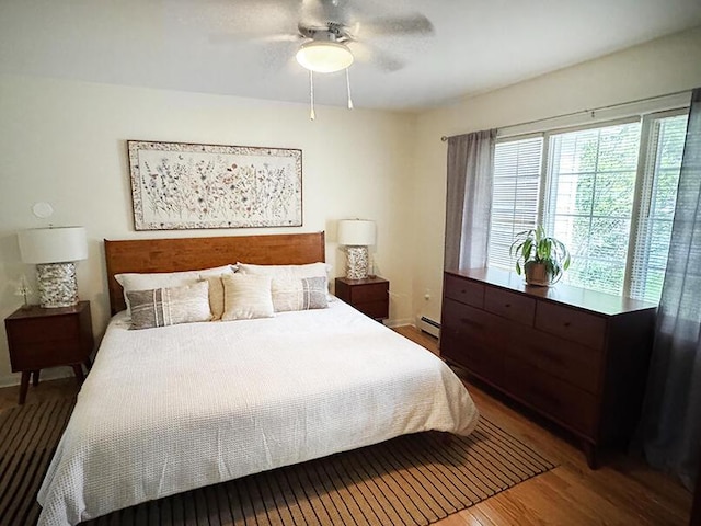 bedroom with wood finished floors, a baseboard radiator, baseboards, and a ceiling fan