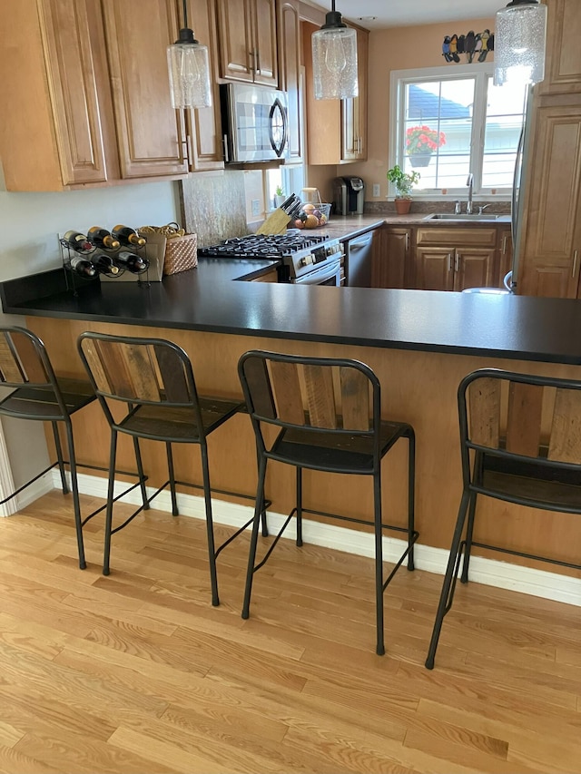 7 Fiddlehead Fern Trl Unit 7, Brunswick, ME 04011 - kitchen with appliances with stainless steel finishes, a sink, light wood finished floors, a peninsula, and a kitchen bar