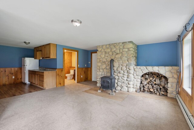 20 Motorcycle Dr, Windham, ME 04062 - unfurnished living room with a baseboard radiator, healthy amount of natural light, a wood stove, wood walls, and a wainscoted wall