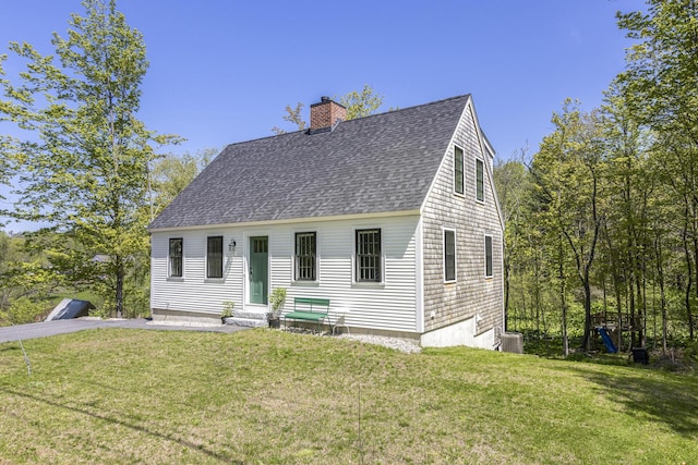 cape cod-style house featuring roof with shingles, a chimney, a front yard, and entry steps