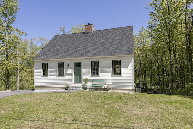 cape cod-style house featuring a shingled roof, a chimney, entry steps, and a front lawn