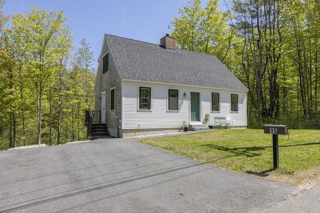 new england style home featuring roof with shingles, a chimney, entry steps, and a front lawn