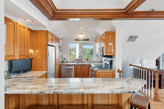 15 Christensen Ln Unit A1, Kennebunk, ME 04043 - kitchen featuring stainless steel appliances, vaulted ceiling, light stone counters, brown cabinetry, and a kitchen breakfast bar