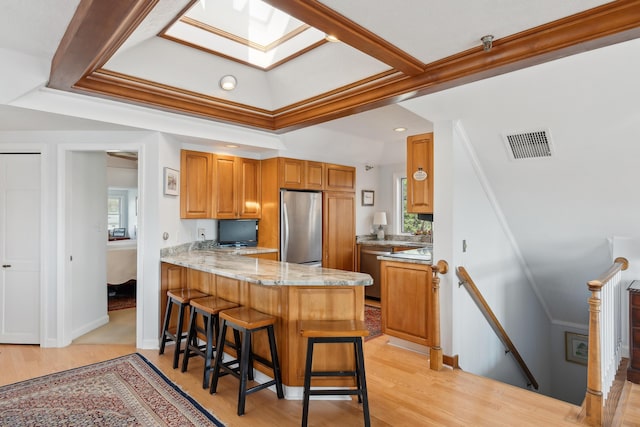 15 Christensen Ln Unit A1, Kennebunk, ME 04043 - kitchen with freestanding refrigerator, crown molding, a breakfast bar area, brown cabinets, and a peninsula