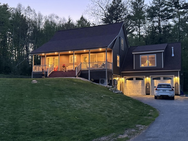 view of front of house featuring a garage, asphalt driveway, a lawn, and a porch