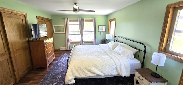 bedroom featuring dark wood finished floors, a baseboard heating unit, ceiling fan, and two closets