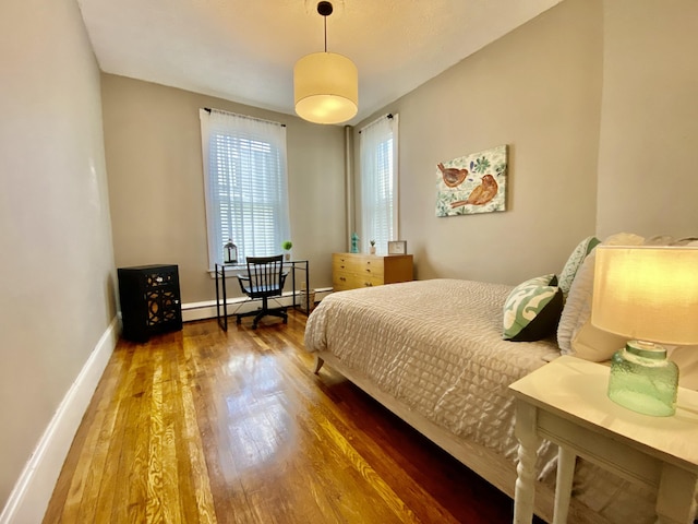 bedroom with wood finished floors, a baseboard heating unit, and baseboards